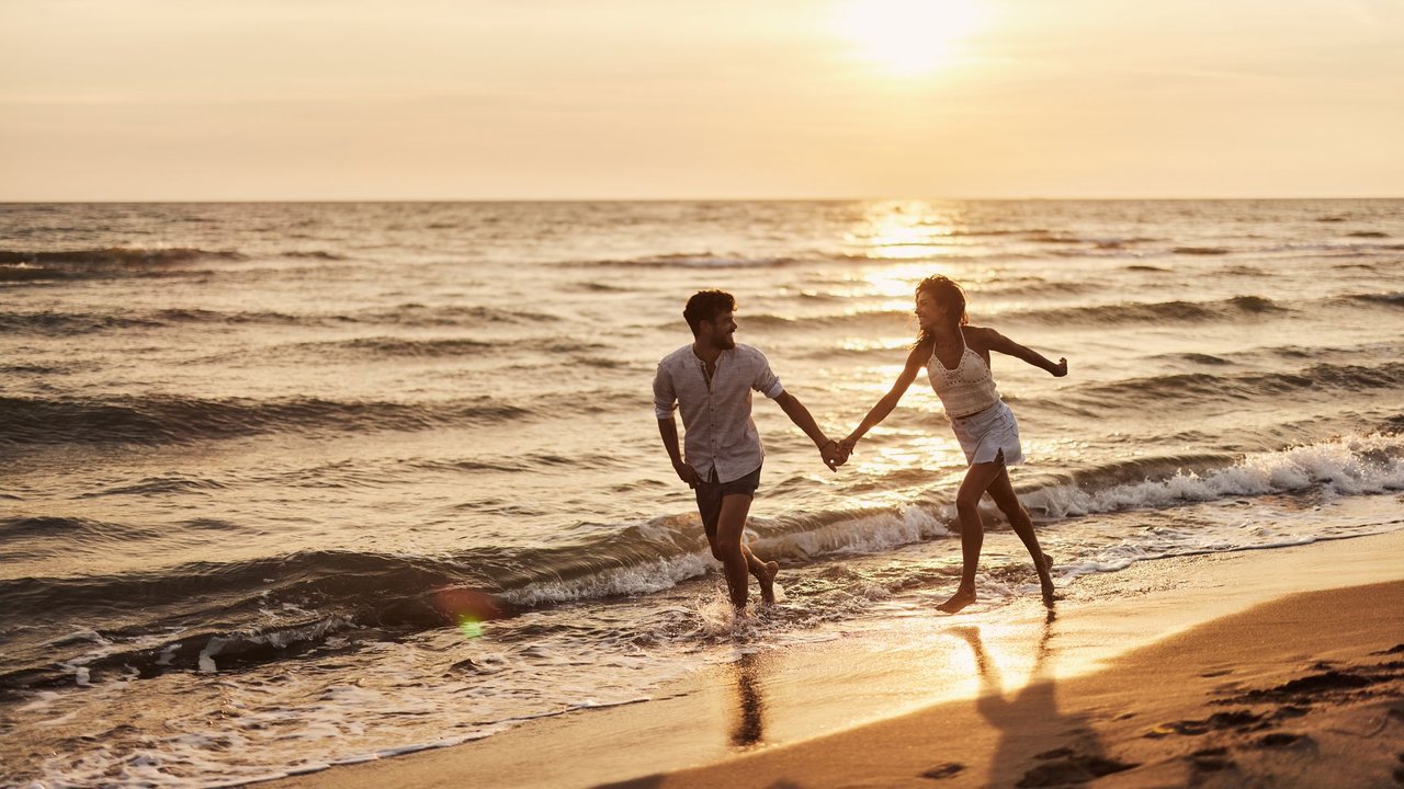 Junges fröhliches Paar läuft im Sonnenuntergang am Strand