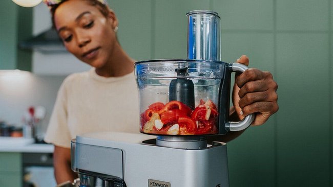 Eine Frau ist auf dem Bild zu sehen, die eine Paprika mithilfe der Küchenmaschine zubereitet.