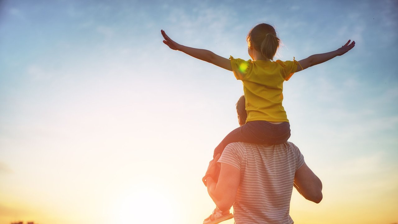 Vater trägt sein Kind auf den Schultern in Richtung Sonnenaufgang