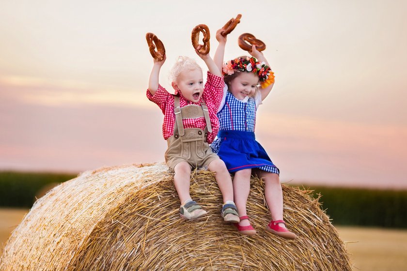 Zwei Kinder mit traditioneller bayerischer Kleidung und Brezeln auf einem Heuballen