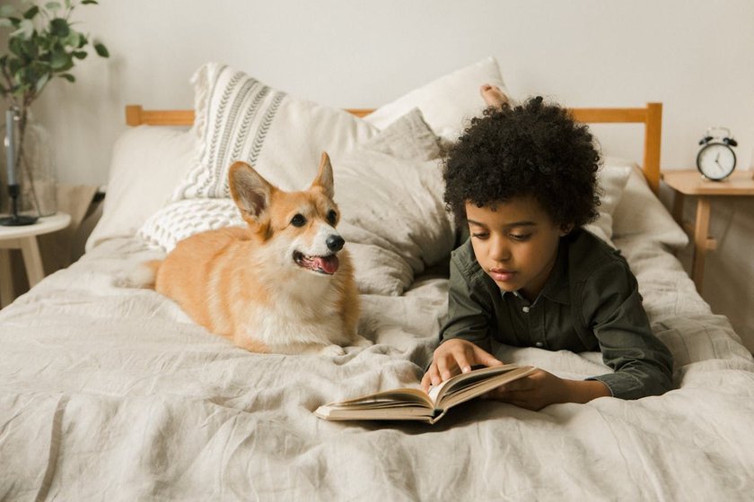 Junge liegt mit einem Hund auf dem Bett und liest. 