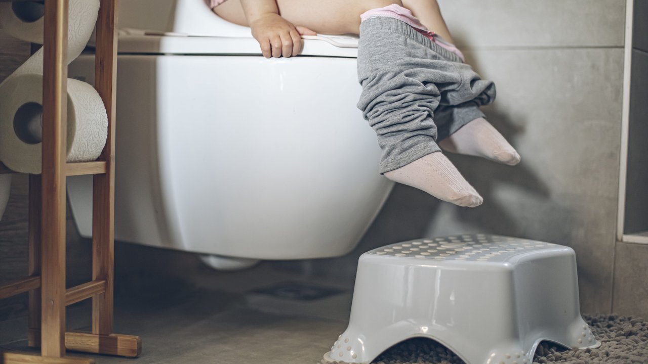 Kind geht mithilfe einer WC-Sitzerhöhung alleine auf die Toilette