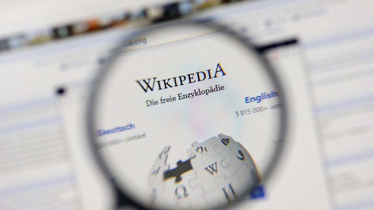Eine Lupe vergrößert das Logo von Wikipedia - Die freie Enzyklopädie