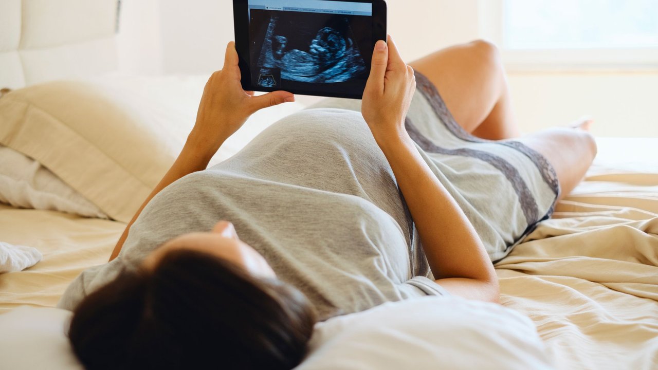 Gebärmutterhals verkürzt: Schwangere liegt im Bett und schaut sich ein Ultraschallbild vom Baby an