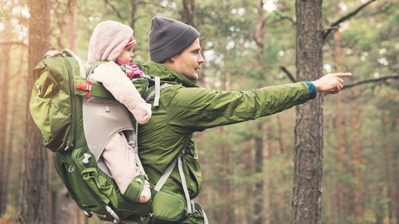 Vater trägt sein Baby in einer Rückentrage durch den Wald