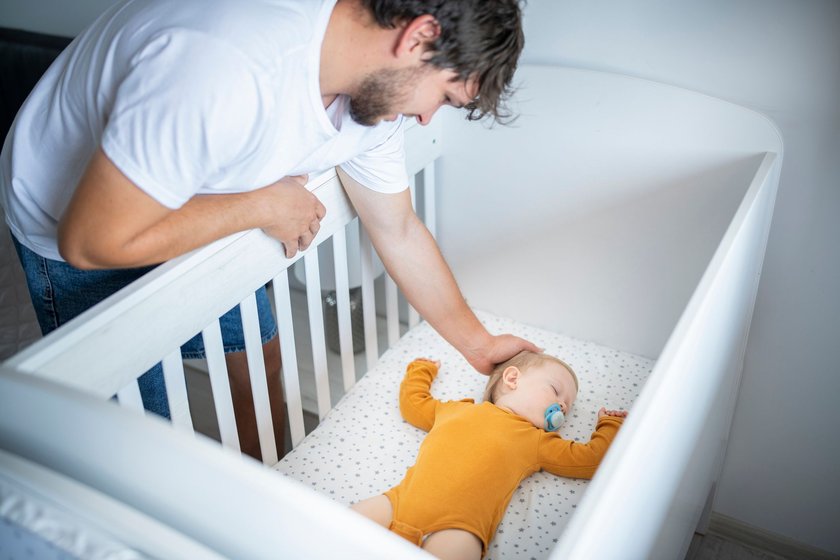 Caring father carefully placing his little boy in the crib for his nap.