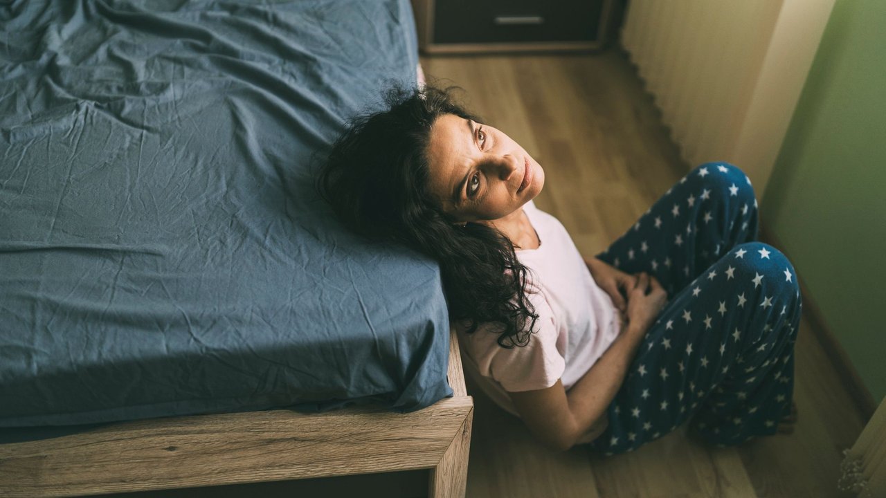 Junge Frau sitzt voller Sorgen neben ihrem Bett und fragt sich, ob Stress zu einer Fehlgeburt geführen kann.