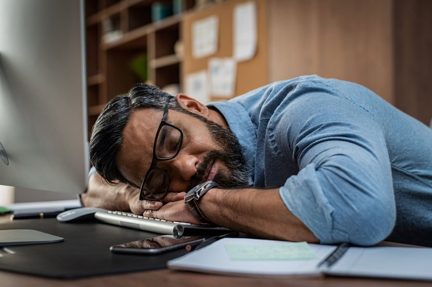 Beamtenwitze: Mann mit Brille und Bart in Jeanshemd liegt in Büro auf Tastatur und schläft