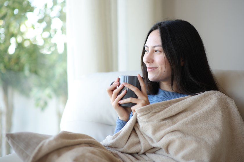 Relaxed asian woman looking through a window keeping warm