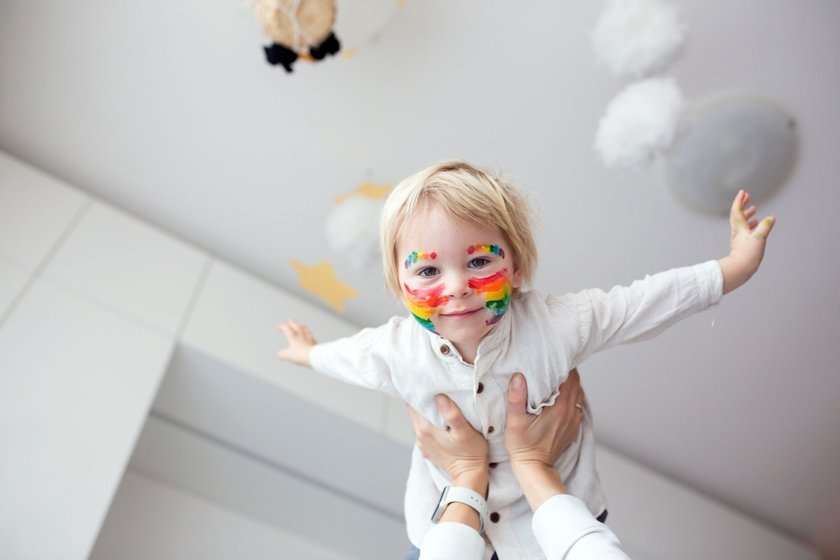 Beautiful blond toddler boy with rainbow painted on his face and messy hands, smiling happily