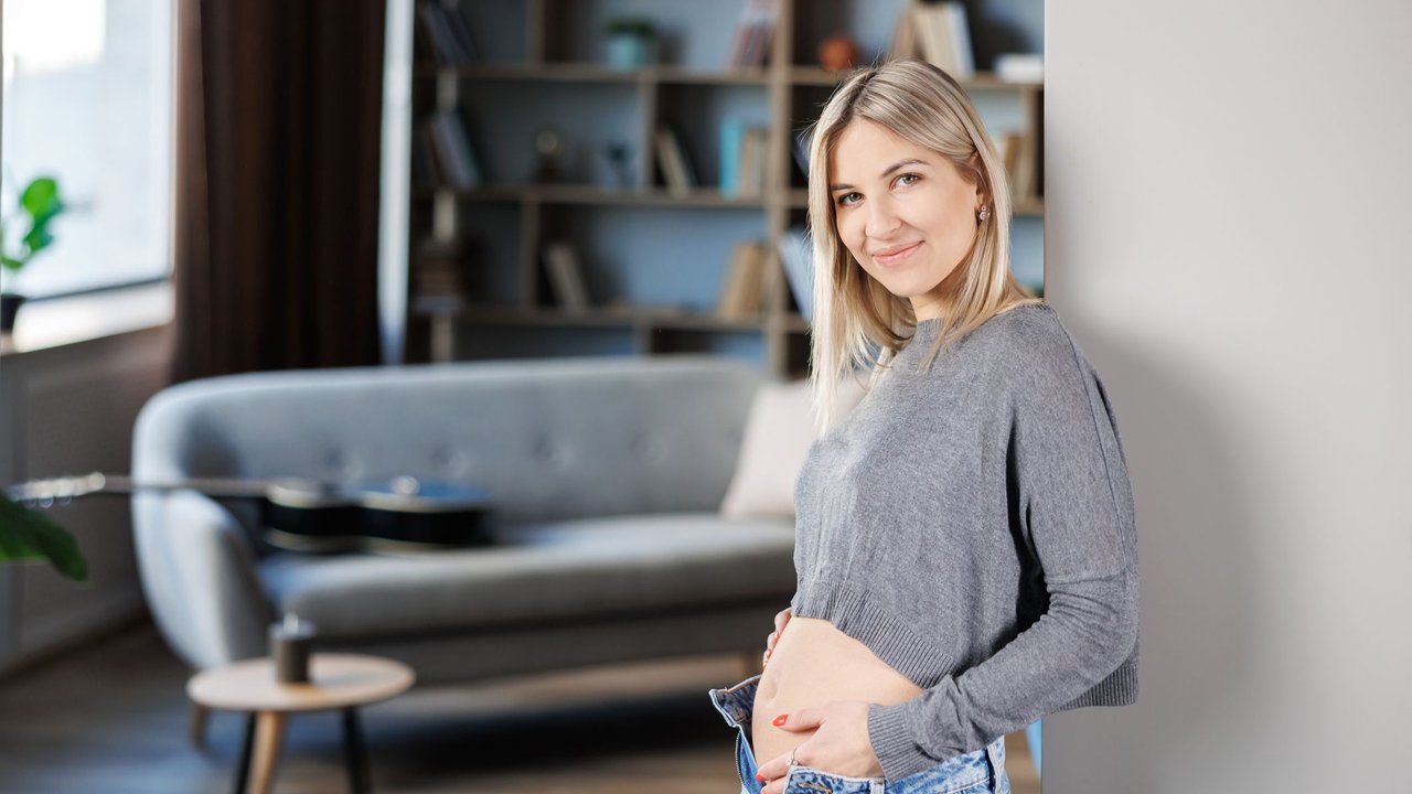 Young beautiful pregnant woman standing near the wall at home.