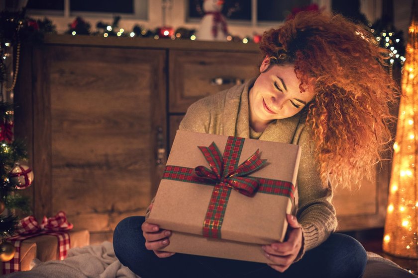 Frau öffnet lächelnd ein Weihnachtsgeschenk