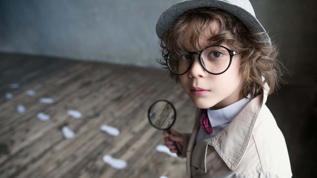 Detektivgeburtstag: Kind mit Hut und Trenchcoat sucht mit Lupe nach Spuren