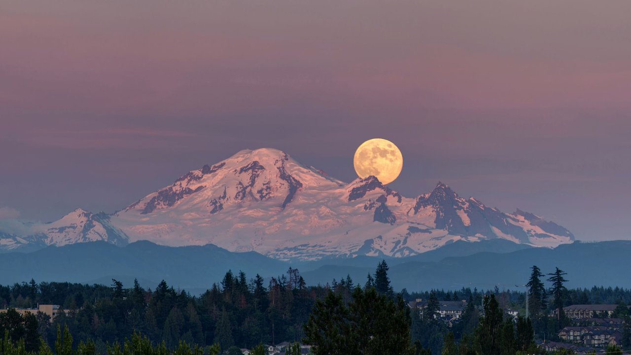 Aufgehender Vollmond über verschneiten Bergen bei Sonnenuntergang