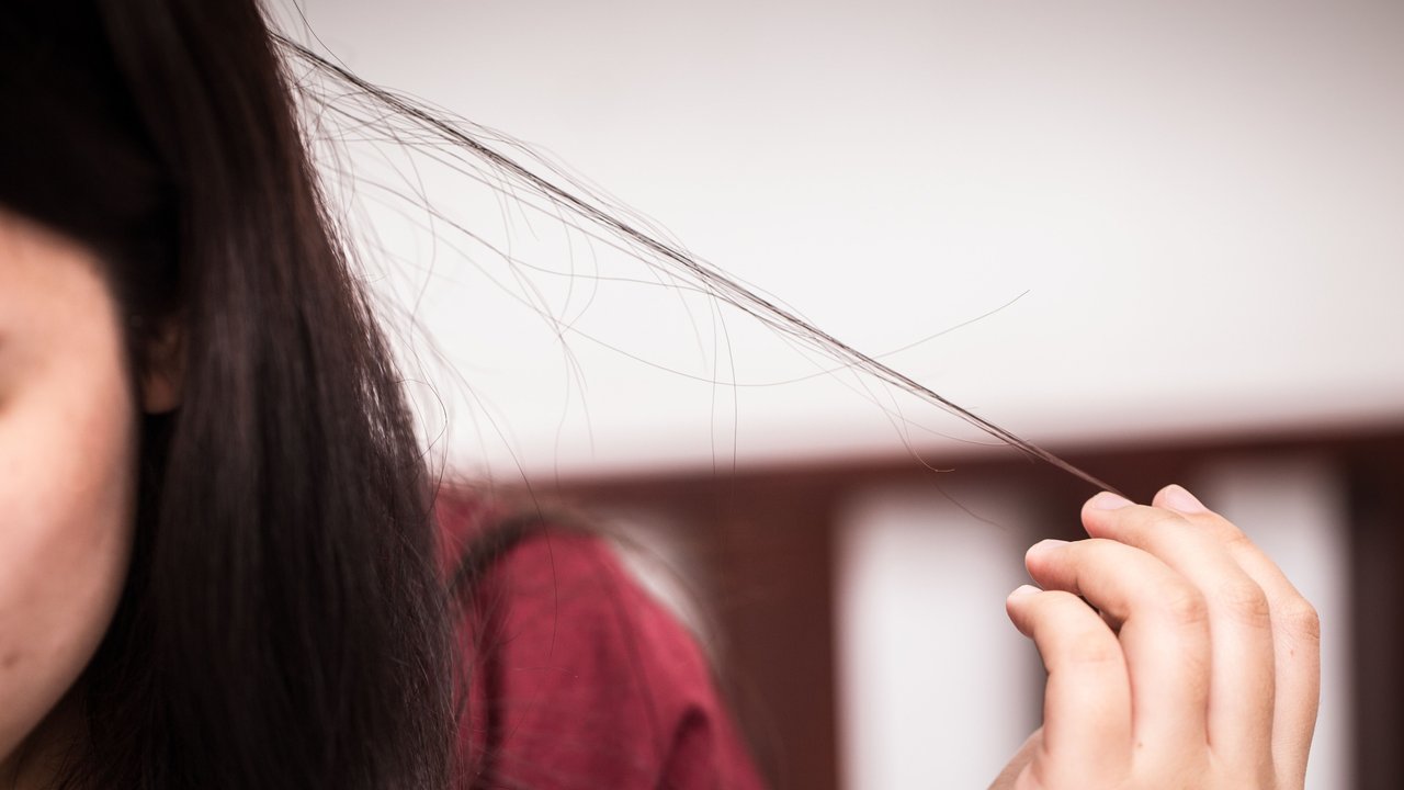 Frau zieht an einer Haarsträhne Trichotillomanie