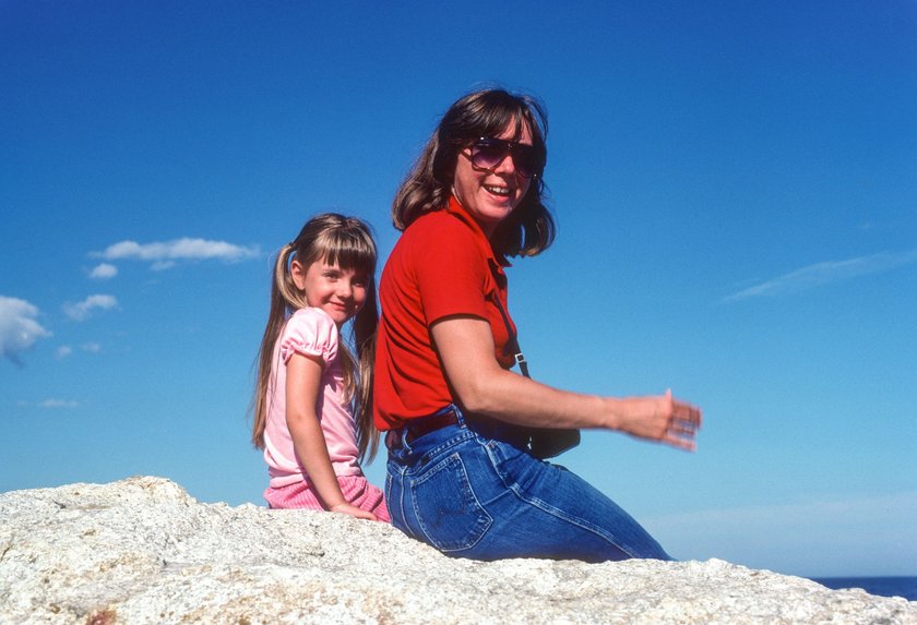 Eine Mama und ihre Tochter sitzen auf einem Stein am Strand