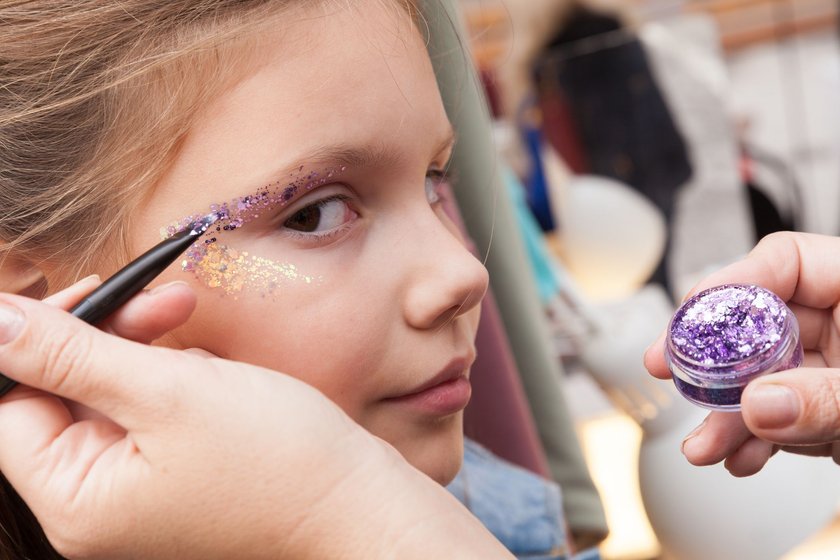 Little girl face makeup applying with colorful glitter