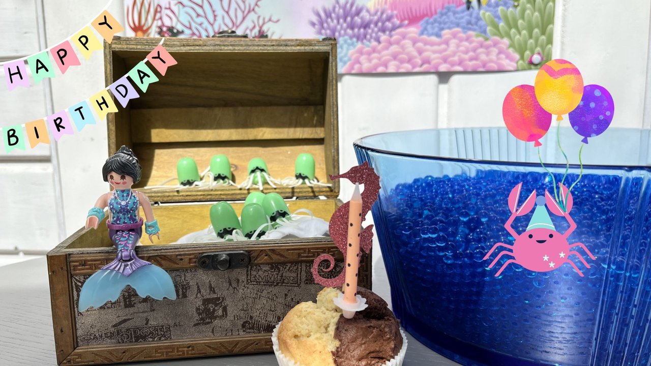 Meerjungfrauen-Geburtstag: Meerjungfrau-Figur sitzt auf Schatzkiste mit Kuchen und Seepferdchen plus Krabbe in Wasserperlen mit Happy-Birthday-Wimpelkette