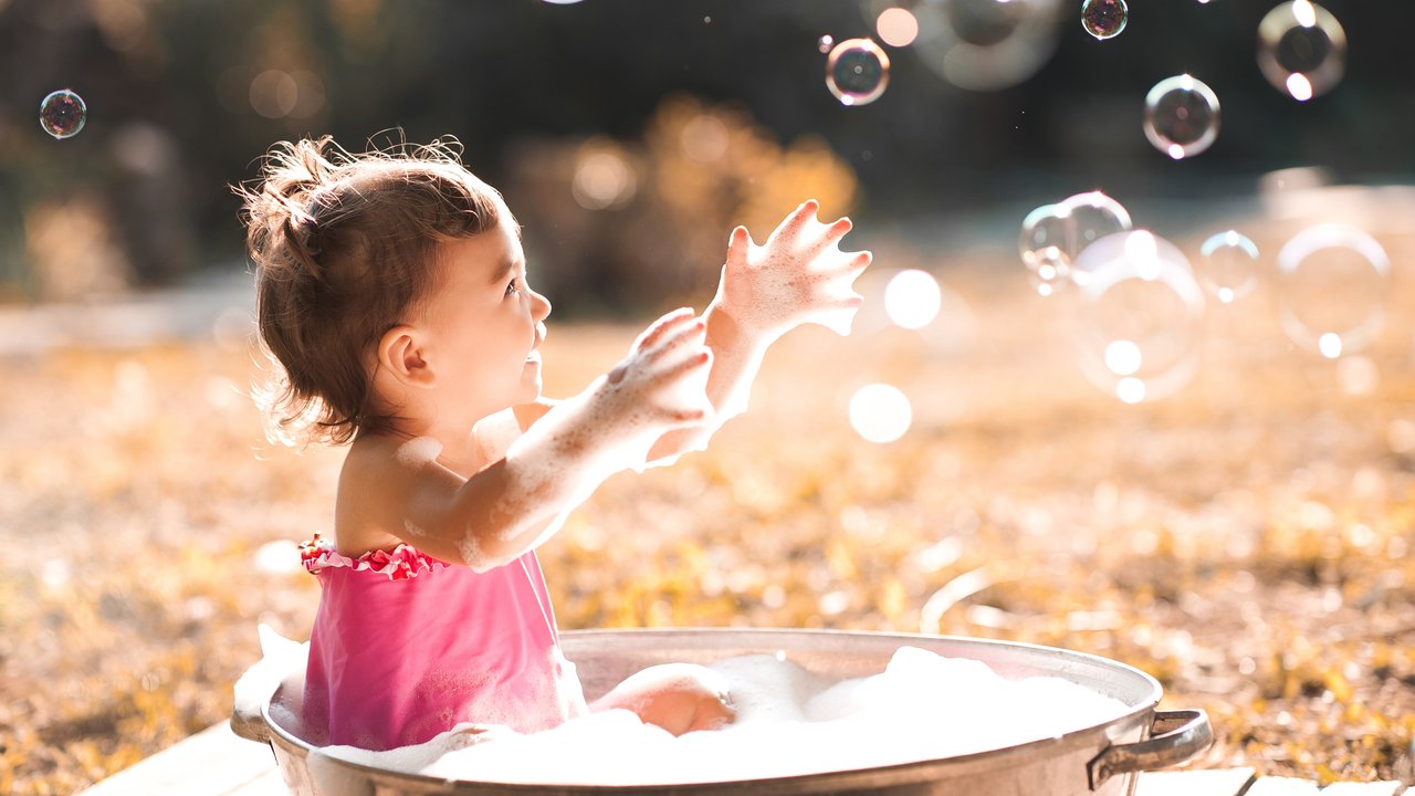 Sonnencreme Baby: Kleinkind sitzt in großem Wassertopf mit Seifenblasen bei Sonnenschein