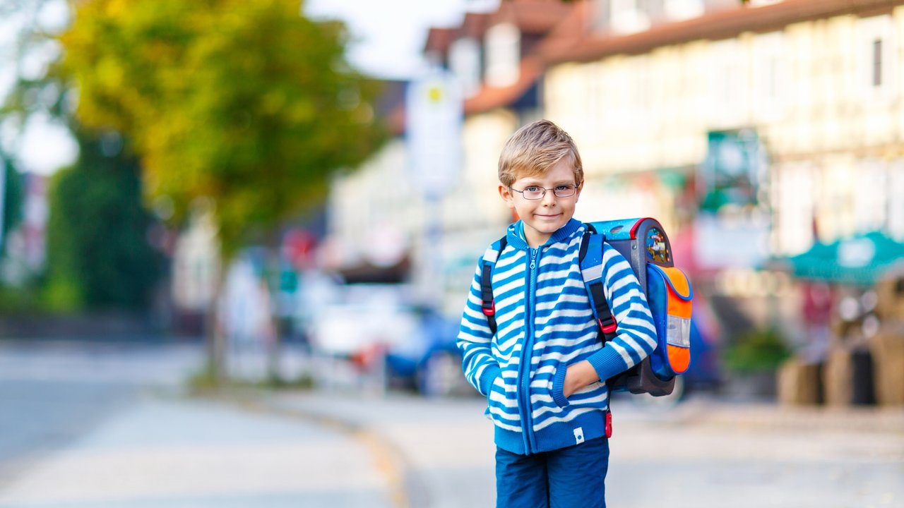 Happy little kid boy with glasses and backpack or satchel on the way to school or nursery. Child outdoors on warm sunny day, Back to school, education concept