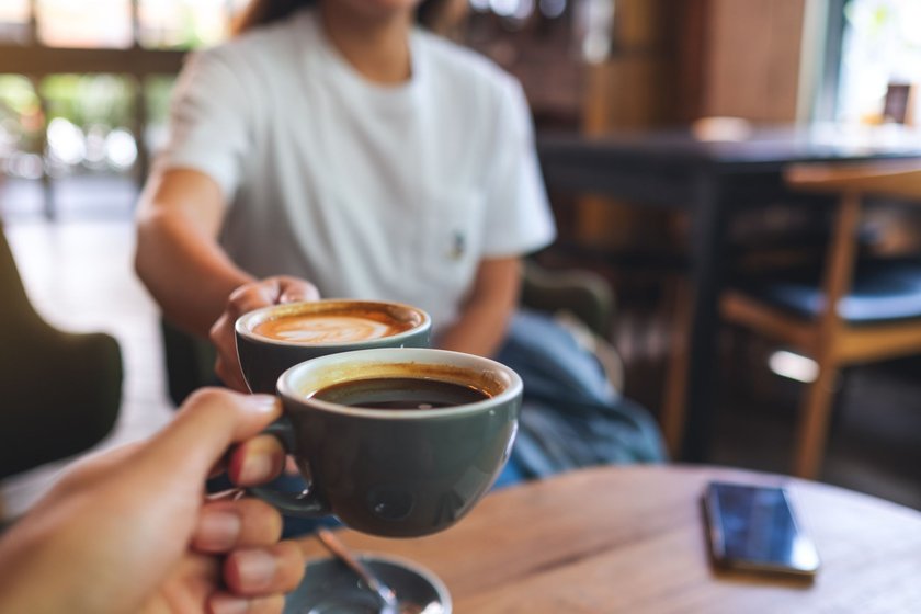 Zwei Personen stoßen in einem Kaffee mit Kaffeetassen an