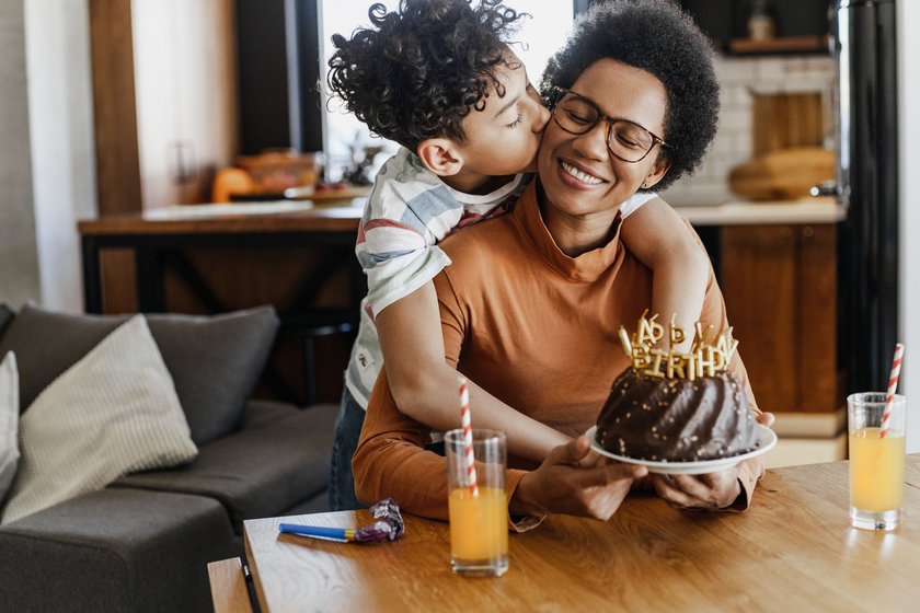 Glückwünsche zum Geburtstag Frau: Mutter wird von Sohn umarmt und bekommt einen kleinen Kuchen überreicht