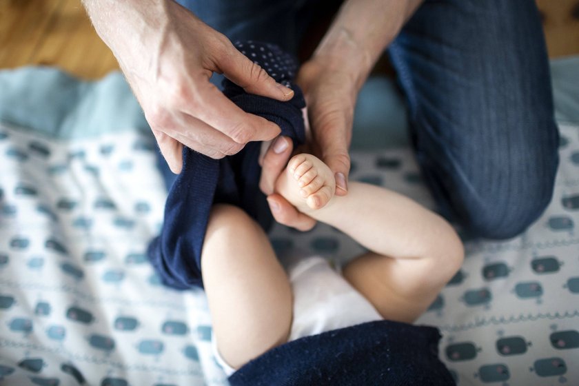 Symbolfoto: Ein Vater zieht ein Baby an.