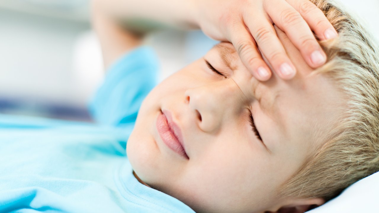 Close-up of little boy with headache, holding his head with his hand.