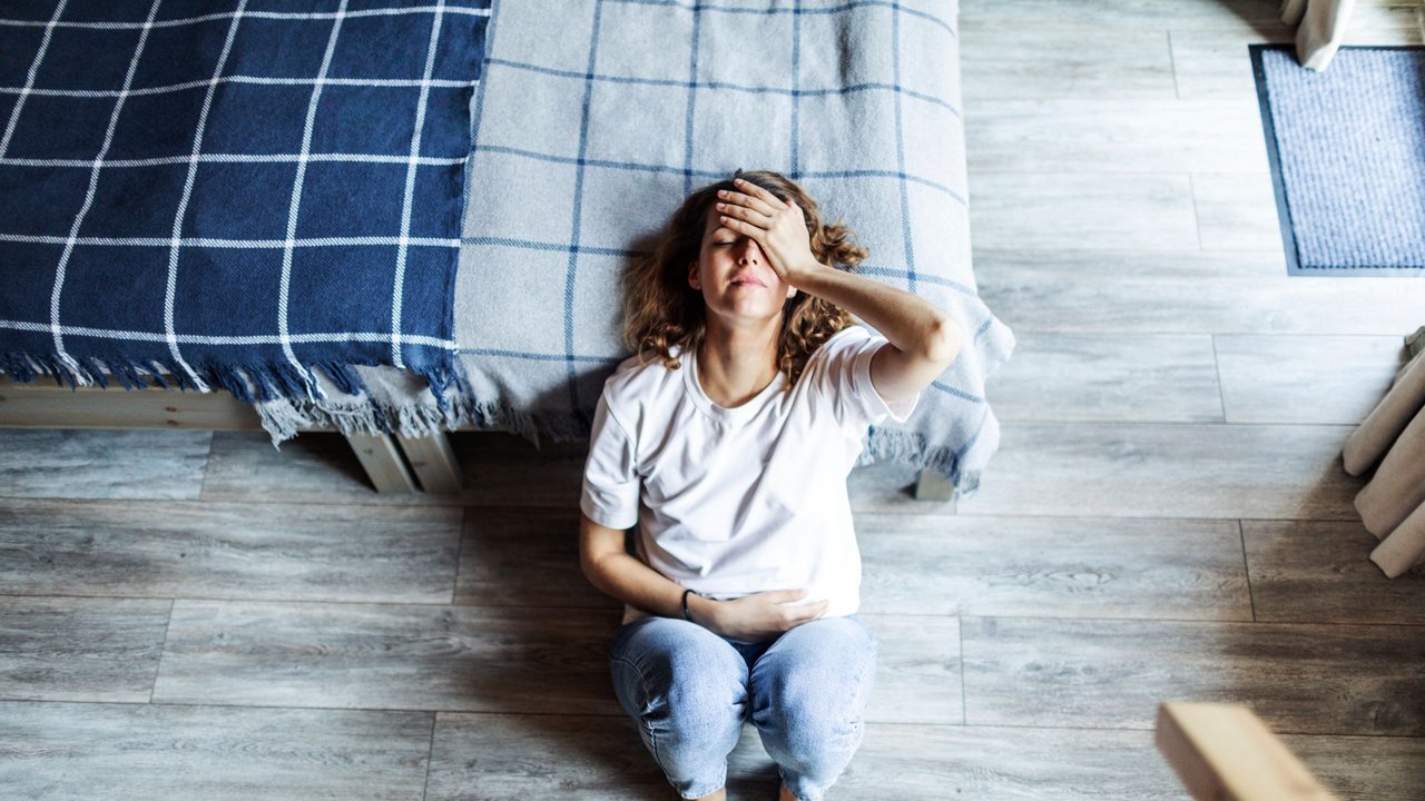 Frau liegt verzweifelt vor ihrem Bett und fragt sich, ob sie Anzeichen einer Fehlgeburt verspürt.