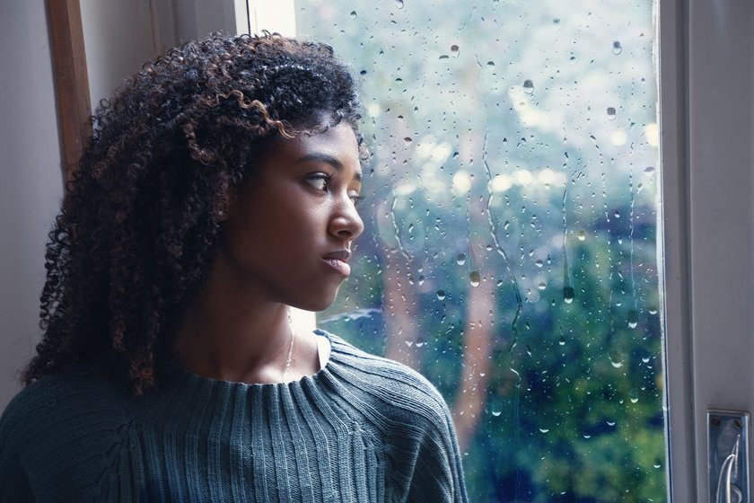 Frau steht am Fenster mit Regentropfen