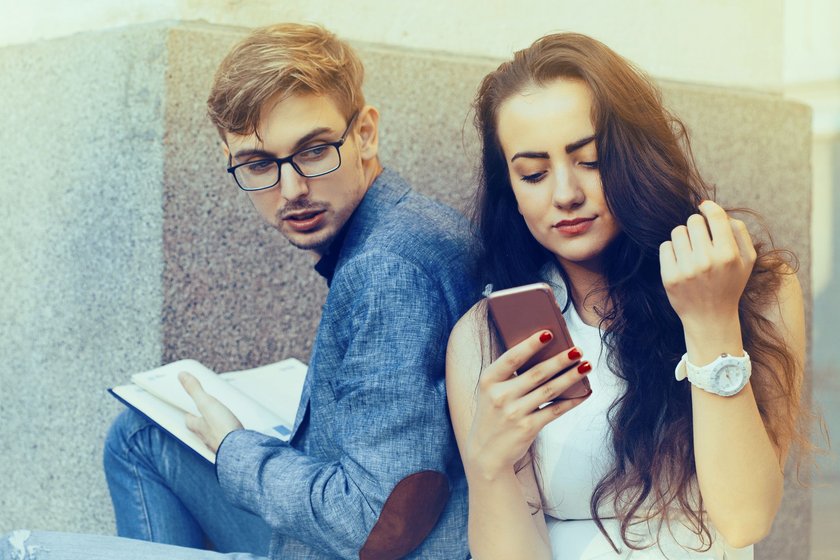 Untreue-Anzeichen in einer Beziehung: Mann schaut heimlich aufs Handy seiner Partnerin