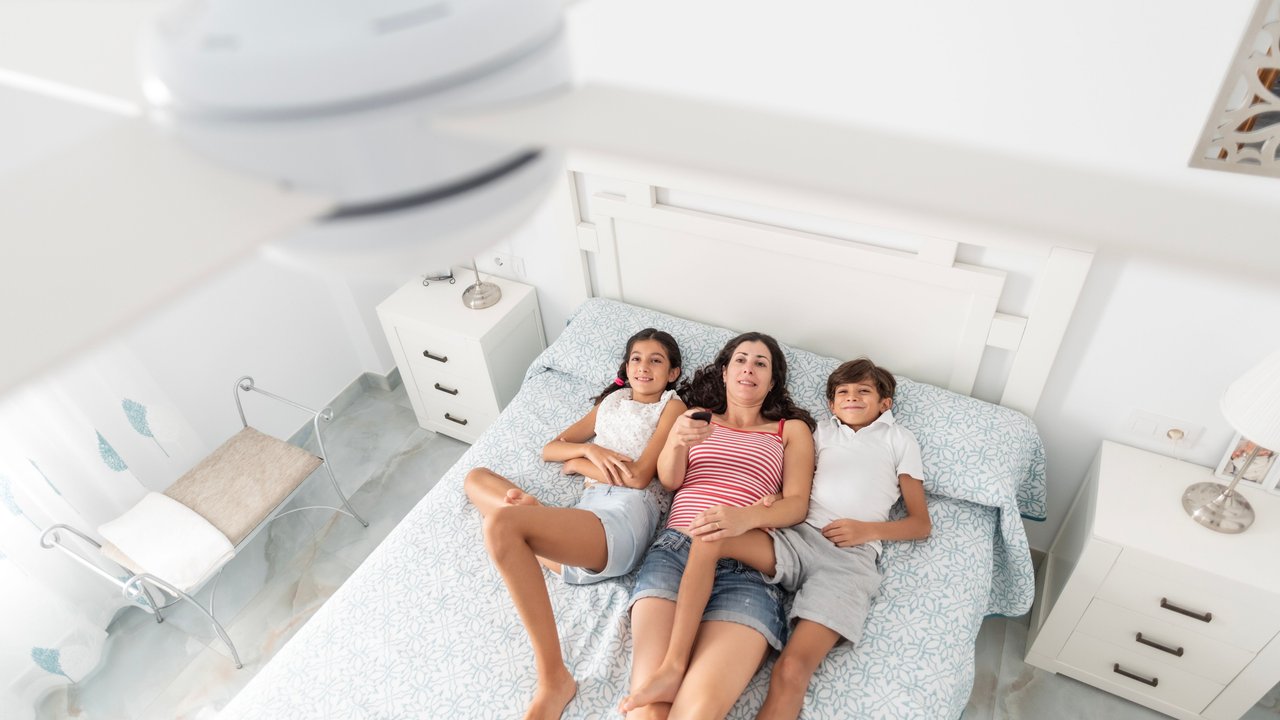 Mama liegt mit ihren zwei Kindern unter einem Deckenventilator