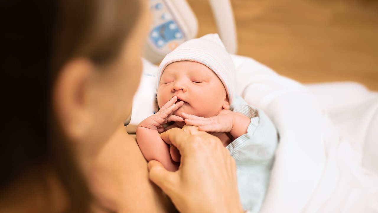 Geburtsbescheinigung: Mutter hält Neugeborenes im Krankenhausbett im Arm