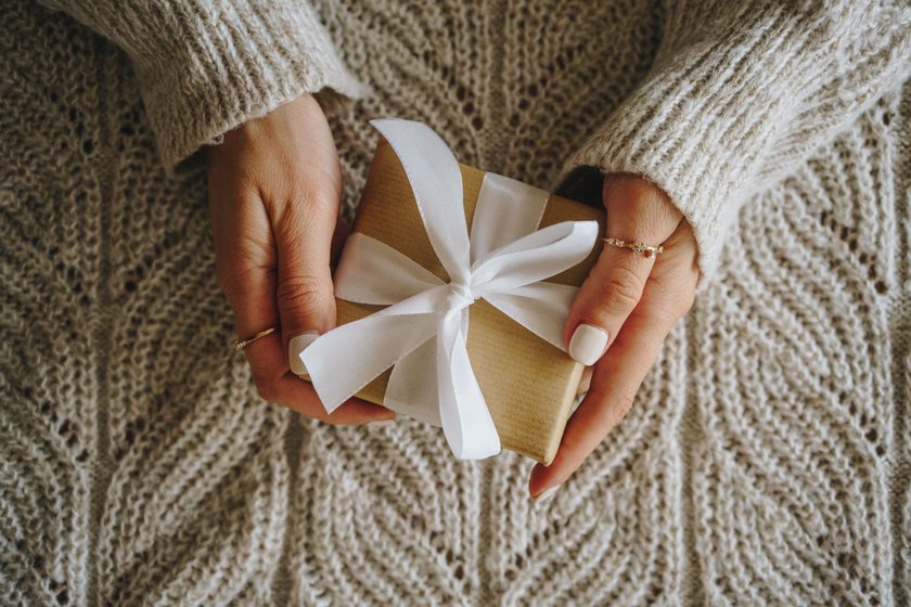 Woman holding a Christmas gift box on cozy knit blanket