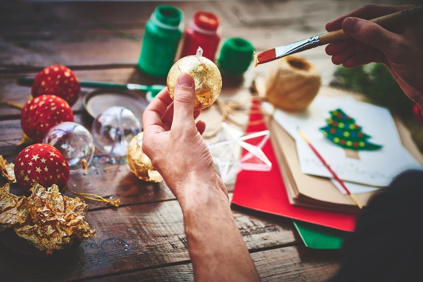 Mann bemalt Weihnachtsbaumkugeln mit Gold