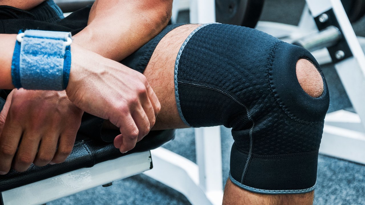 Mann trägt Knie-Bandage im Fitnessstudio