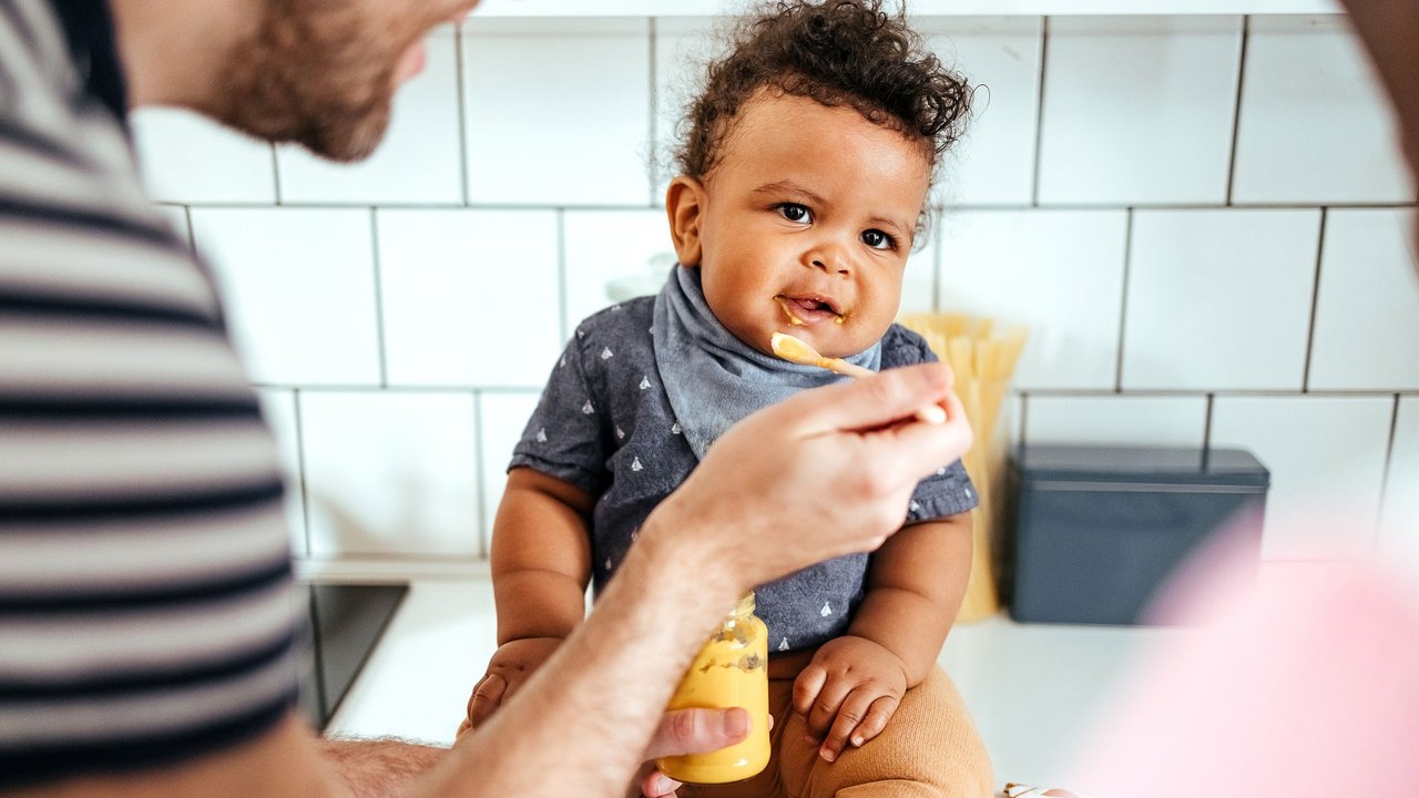 Getreidebrei Baby: Papa füttert Baby mit Obst-Getreidebrei