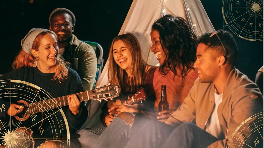 Freundesgruppe sitzt am Lagerfeuer, lacht und spielt Gitarre