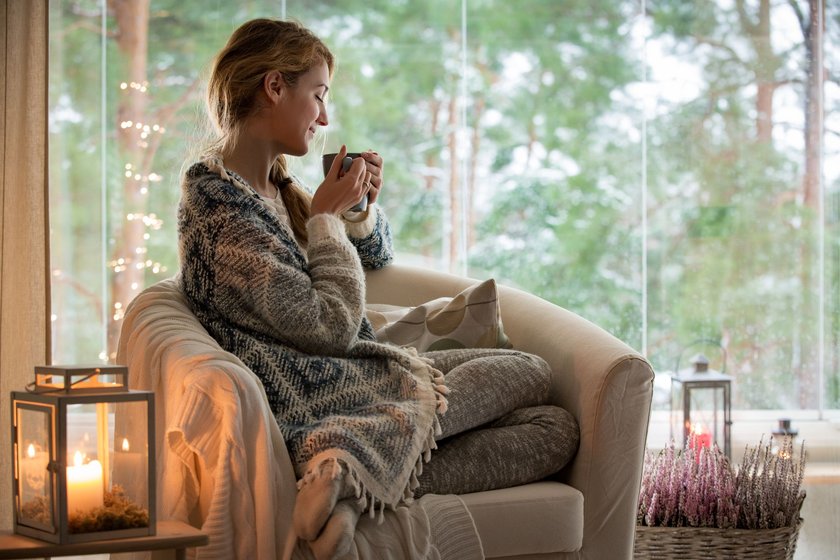 Junge Frau sitzt mit Wolldecke am Fenster