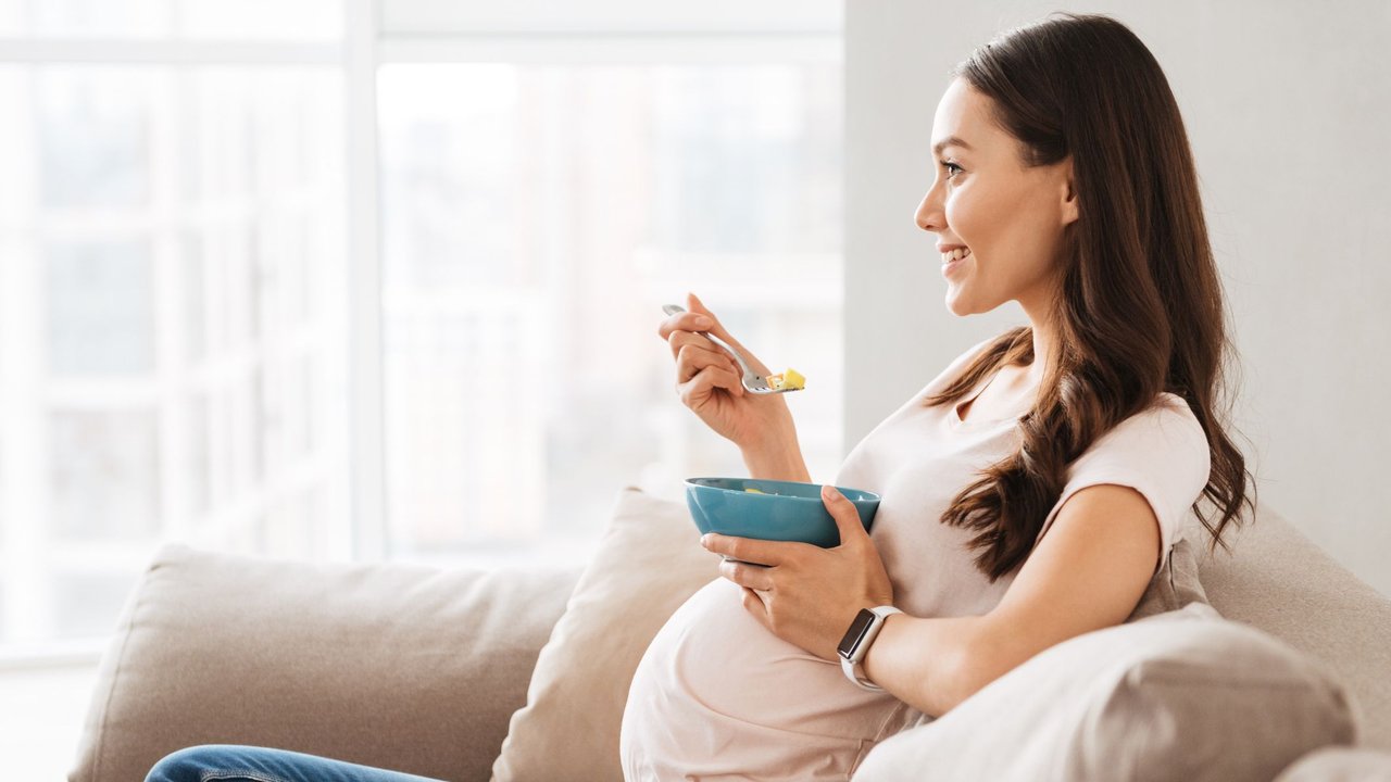 Frühstück Schwangerschaft: Schwangere isst etwas auf der Couch