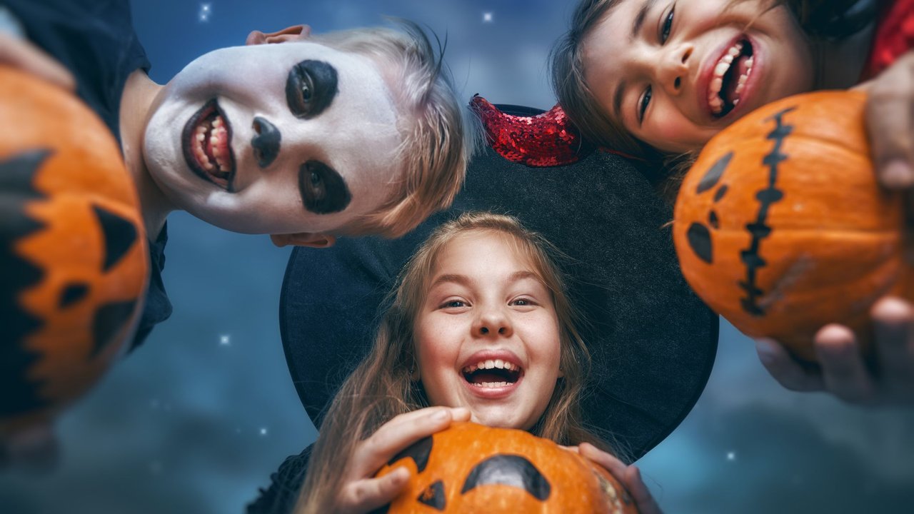 Happy brother and two sisters at Halloween. Funny kids in carnival costumes outdoors. Cheerful children and pumpkins buckets on night sky background.