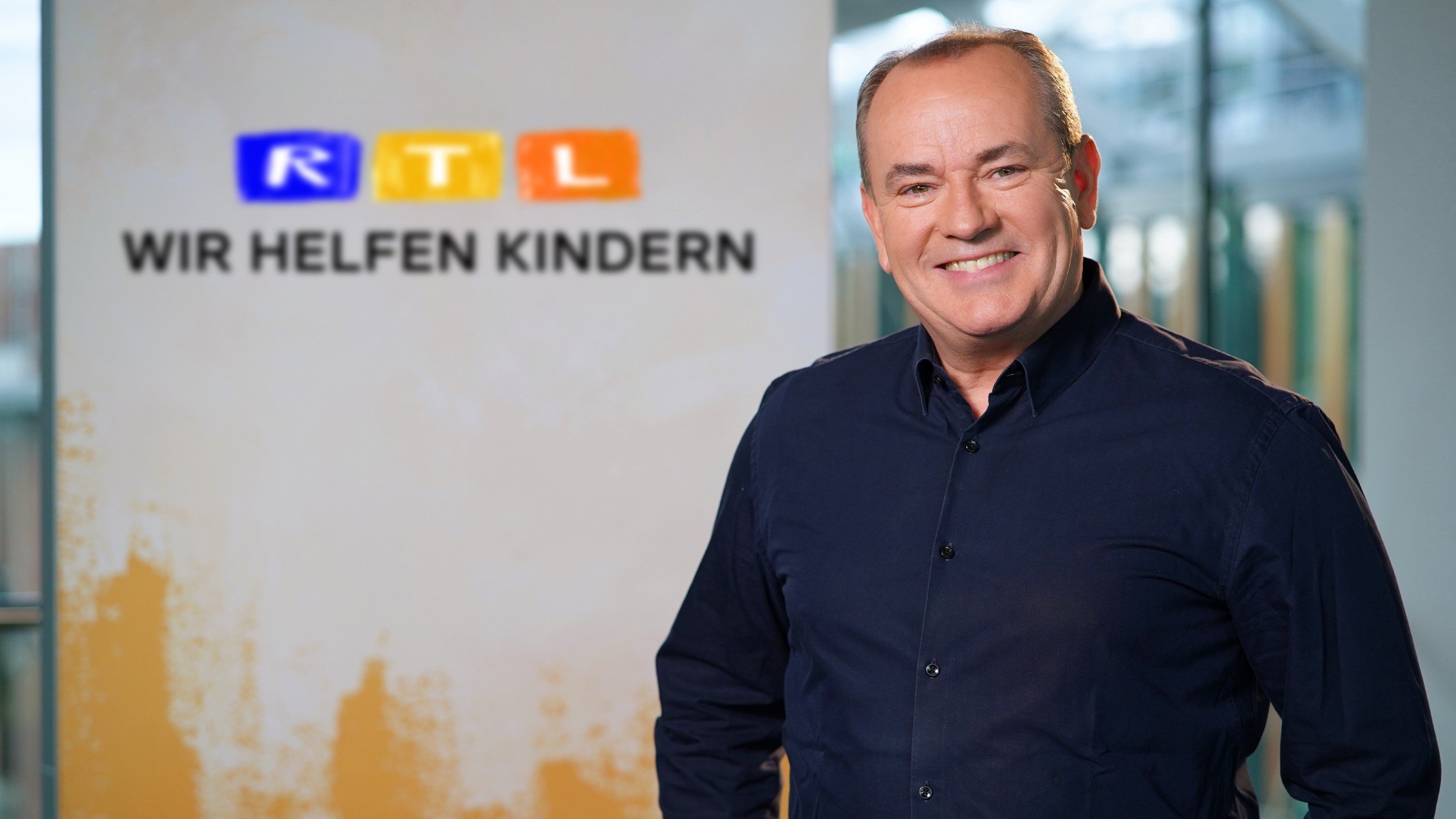 Wolfram Kons vor dem Logo von RTL Wir helfen Kinder