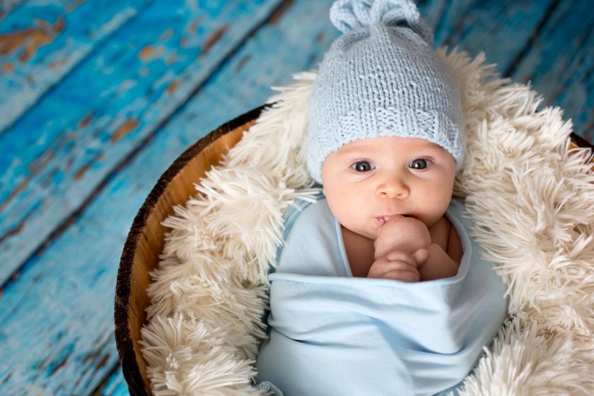 Little baby boy with knitted hat in a basket, happily smiling and looking at camera, isolated studio shot