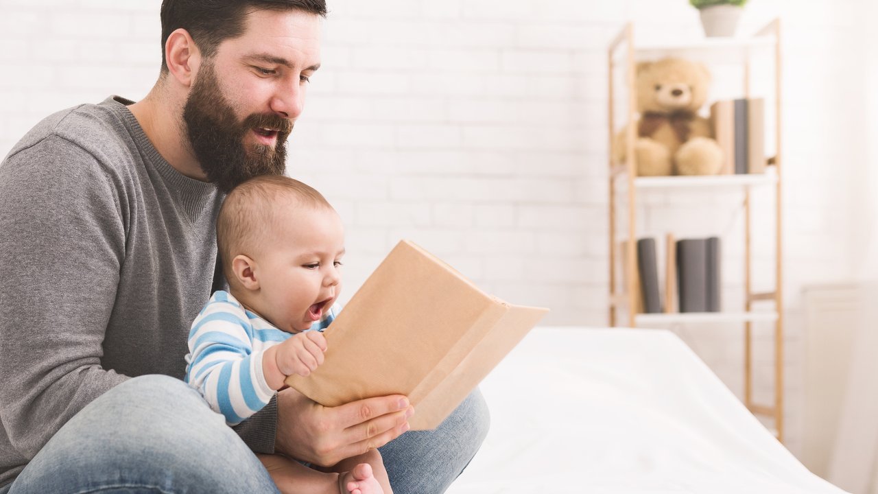 Early development. Adorable infant reading book with daddy, spending time together at home