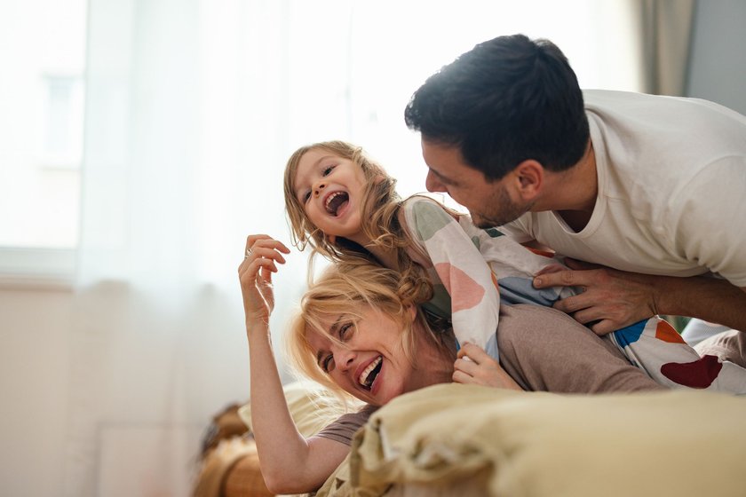 Eine glückliche Familie tobt zusammen auf dem Bett.