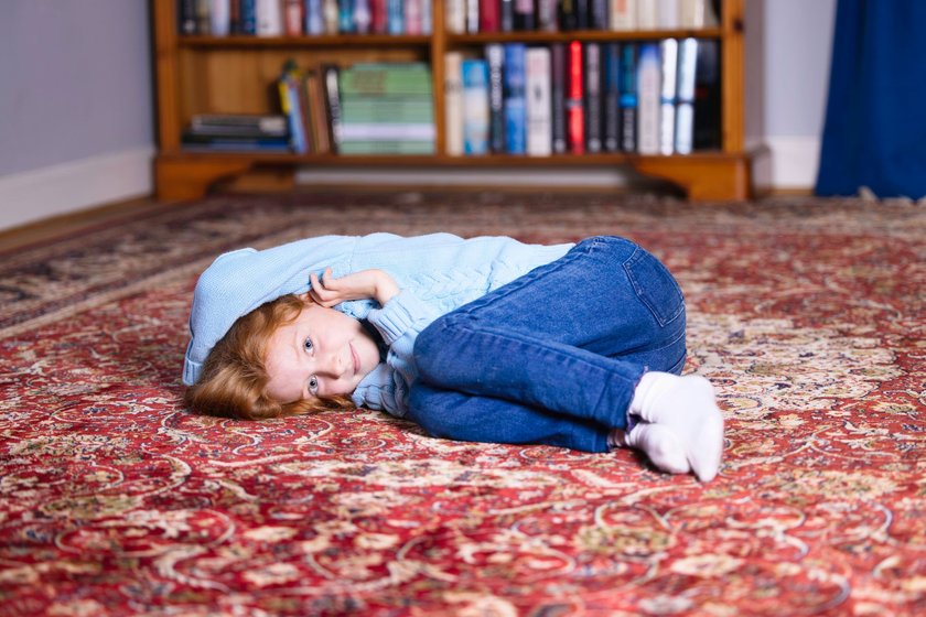 Kind liegt auf dem Teppich und hat Langeweile