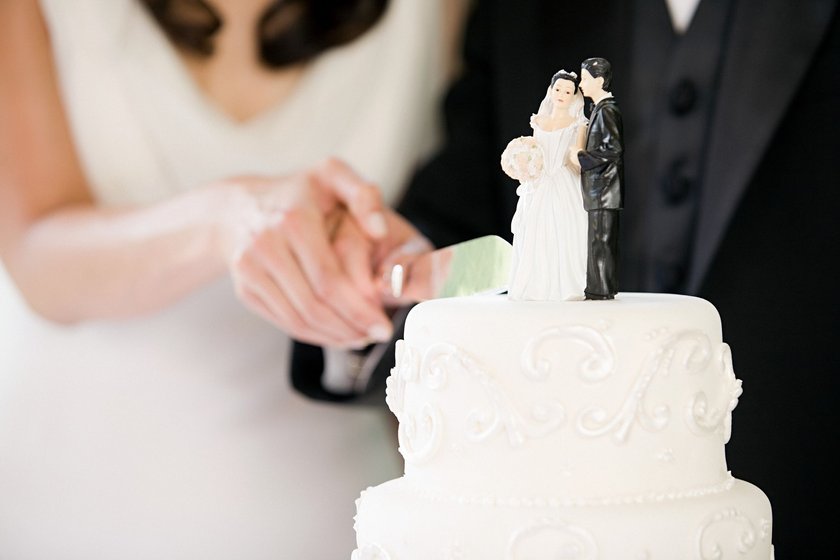 Ein Paar schneidet die Hochzeitstorte mit zwei Mini Figuren an