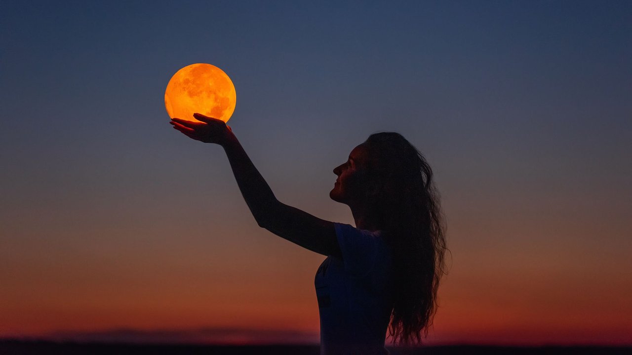 Junge Frau hält einen glühenden Mond am Himmel in den Händen