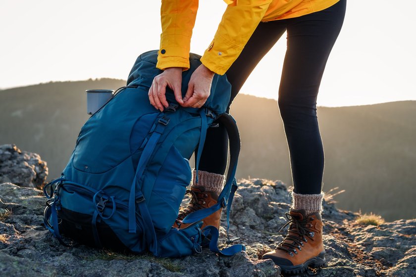 Frau öffnet Rucksack auf einem Berg beim Wandern