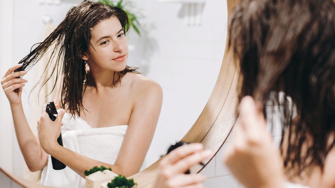 Junge Frau sprüht sich Leave-in-Conditioner in die Haare